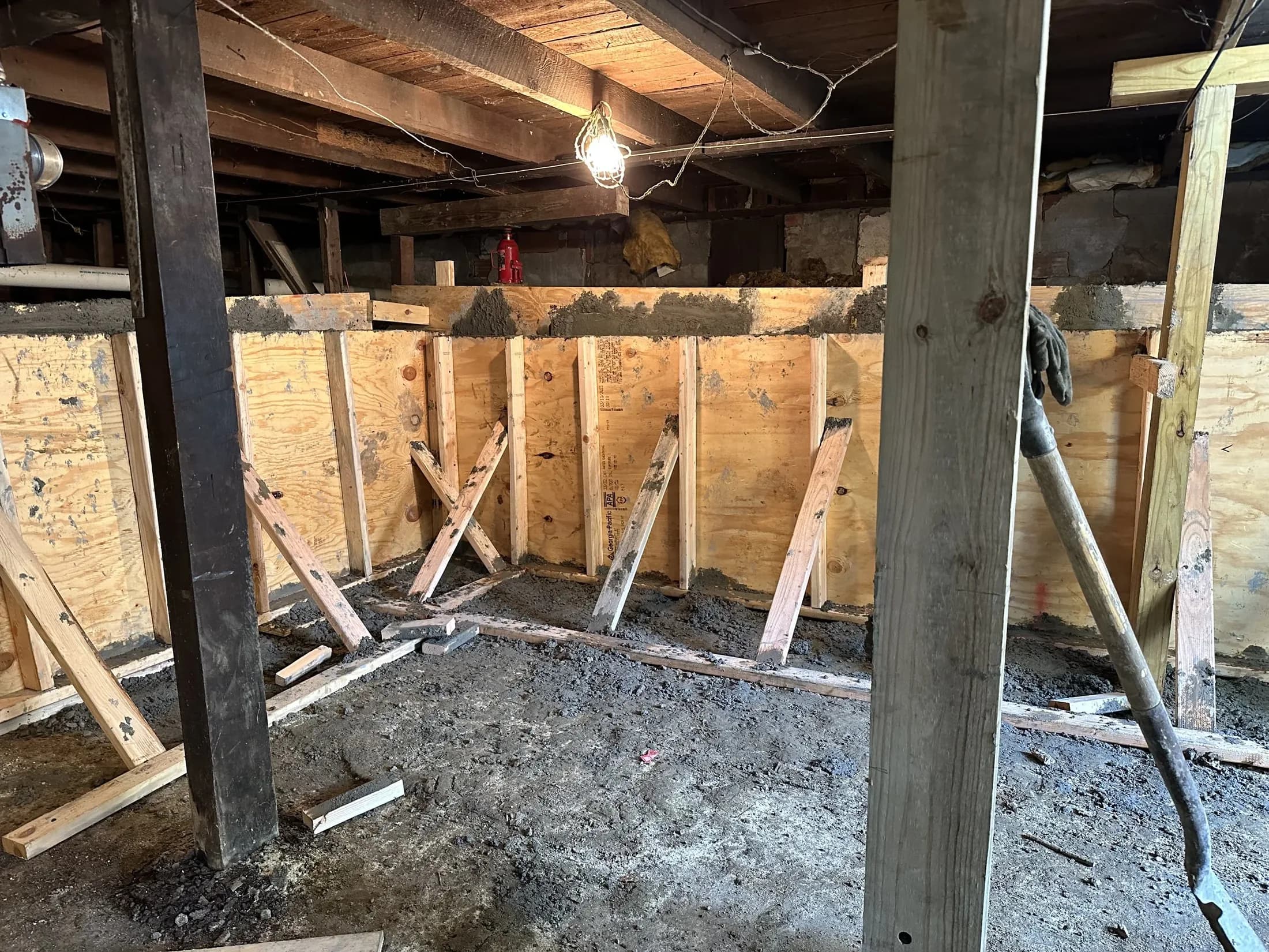 Basement wall rebuilt with braced plywood forms and a fresh concrete cap, under exposed floor joists